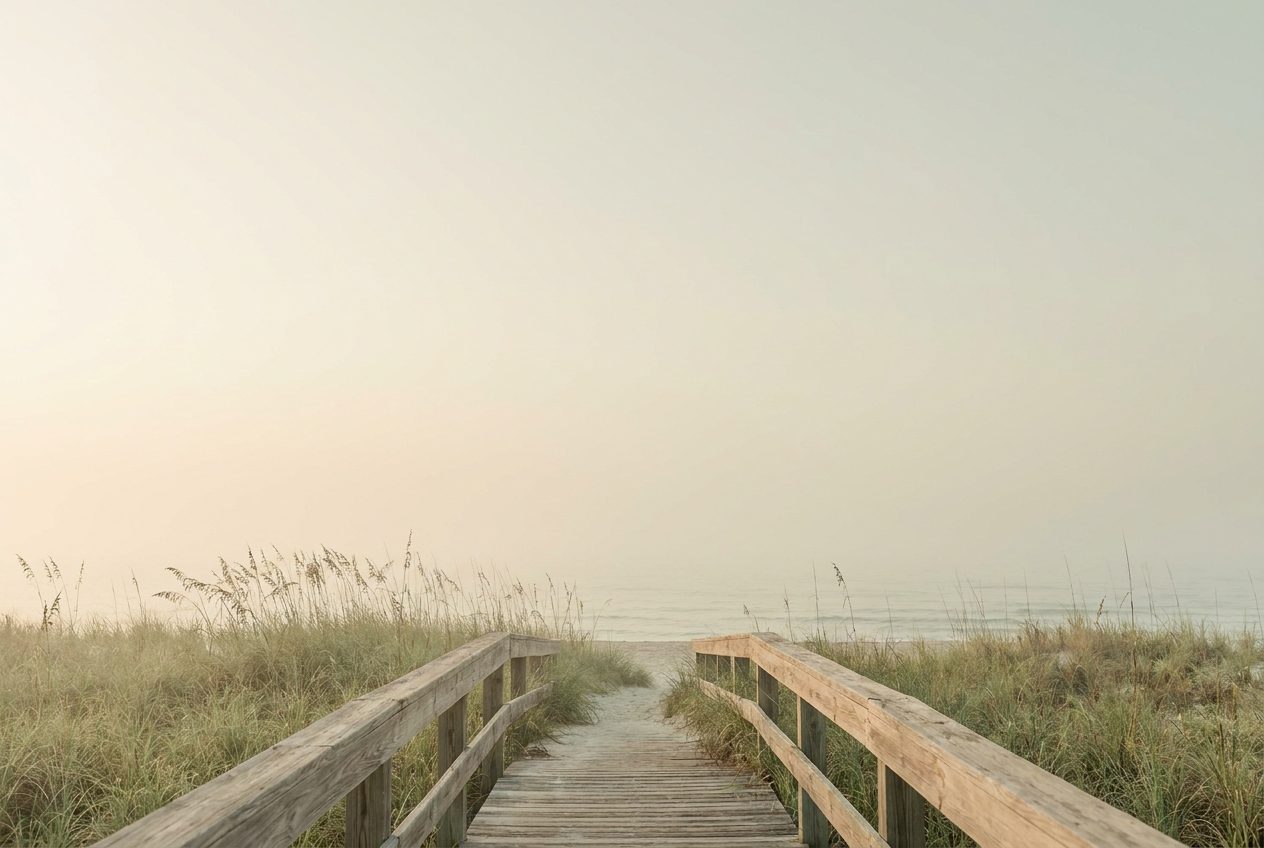 A wooden boardwalk winding through coastal dunes toward calm open water